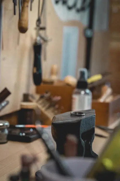 Bague en cours de façonnage posée sur une enclume dans un atelier de bijouterie artisanale, au milieu des outils du travail du métal brut